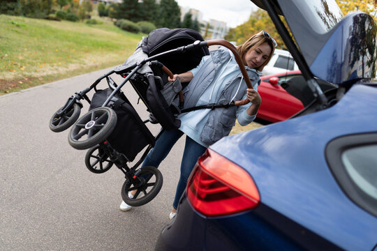 woman loading baby stroller into car trunk