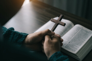 Close up of an open bible with a cross for morning devotion on a wooden table with window lights.