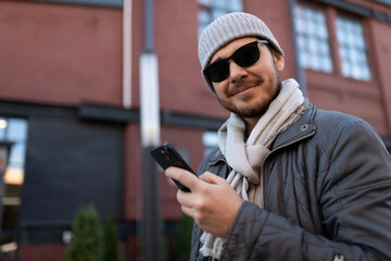 young strong man in a hat and sunglasses with a phone in his hands outside