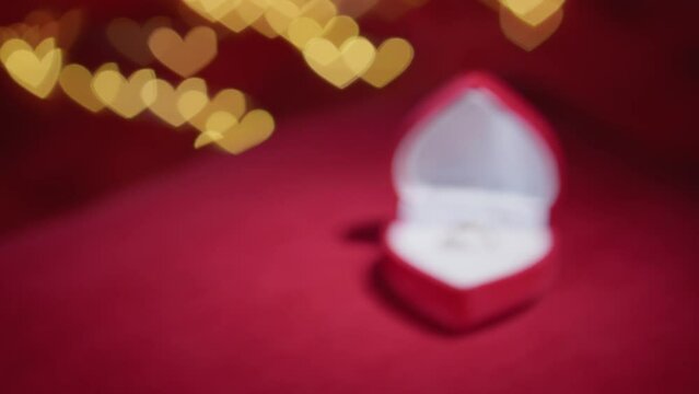 Diamond ring with jewelry gift box on red fabric background. A gold engagement ring for Valentine's Day. Wedding proposal marriage concept. Romantic atmosphere of the holiday and decorations.