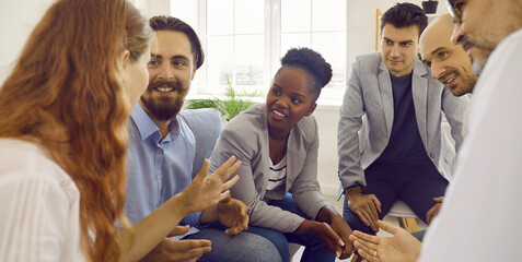 Close up shot of multiracial business people talking together. Smiling colleagues looking at female coworker chatting in office. Happy employees having casual conversation at workplace at break