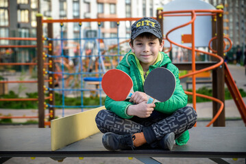Happy ping pong player think about a game. young boy sitting after match on a tennis table outdoors