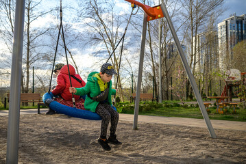 Two little kid boys having fun with swing on outdoor playground. Children, best friends and siblings swinging on warm sunny spring or autumn day. Active leisure with kids. Casual boy fashion