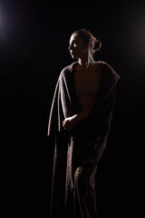 The silhouette of a girl in a veil looking like a statue or sculpture on a black background. A model poses for a photo shoot in the studio