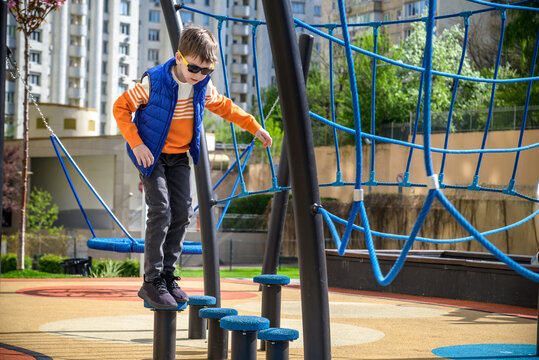 Children's obstacle course on a modern playground. Kid crossing a wooden bridge or other barriers using his body balance. Development of the child's agility and courage