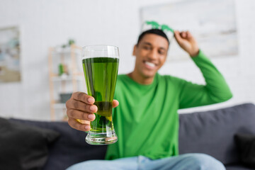 Blurred african american man holding green beer at home