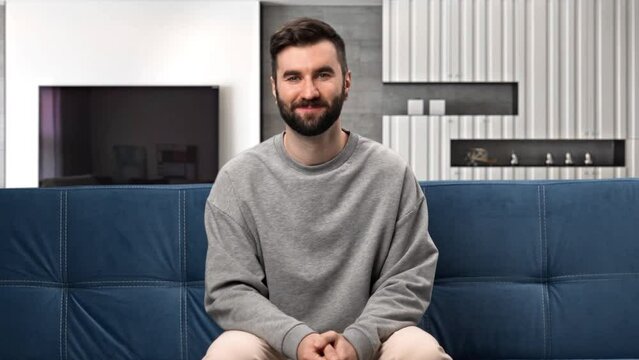 Happy modern bearded man relaxing on comfortable home couch spending time alone apartment interior