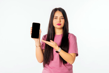 Online shopping. Young woman pointing at her mobile phone screen, showing smartphone app interface, stands against white studio background. Mobile phone with black screen in female hand.