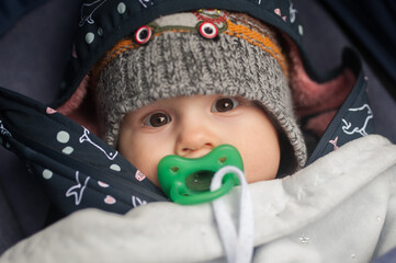 Portrait view of cute little peaceful baby with pacifier in winter jacket and hat. Joy and happiness concept. Love and family emotion