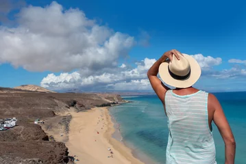 Photo sur Plexiglas Plage de Sotavento, Fuerteventura, Îles Canaries Hombre de espaldas sosteniendo su sombrero de paja frente a la playa de arena blanca y el mar turquesa de Jandia en la localidad turística de Fuerteventura en las Islas Canarias.