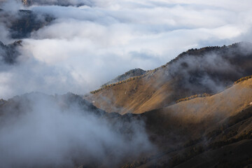 Landscape photo slopes of hills under sunlight and clouds on the background on the plateau Bermamyt. Beautiful trees in autumn colors are on top of the hill in sunlight and a little foggy