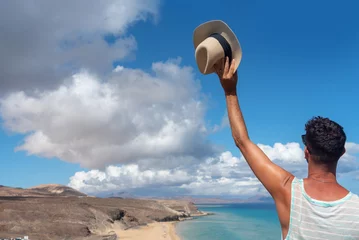 Papier Peint photo autocollant Plage de Sotavento, Fuerteventura, Îles Canaries Turista de espaldas a la playa levantando su sombrero de paja frente a la impresionante playa de arena blanca y el mar turquesa de Jandia en las Islas Canarias.