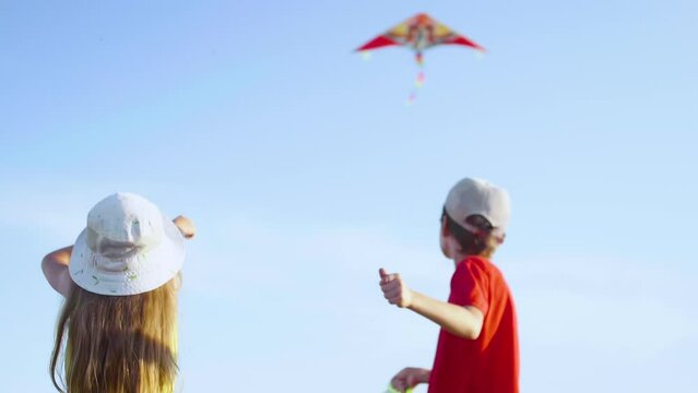 Happy Boy With Little Girl Launches a Colored Kite Into the Blue Sky. Children Having Fun Playing with Kite. Freedom, Childrens Happiness Concept. Carefree Happy Childhood Symbol. Slow Motion.