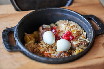 The concept of Oriental cuisine. Uzbek national pilaf with meat in a cast-iron frying pan, on a wooden table. Background image. Top view with copy space. High quality photo