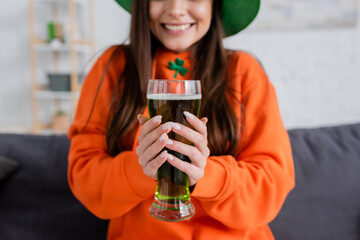 Cropped view of blurred woman holding glass of green beer during saint patrick day