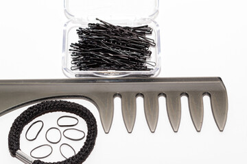 Peine negro con una caja llena de horquillas y gomas de pelo de diferentes tamaños sobre un fondo...