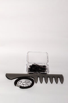 Peine negro con una caja llena de horquillas y gomas de pelo de diferentes tama&ntilde;os sobre un fondo blanco.