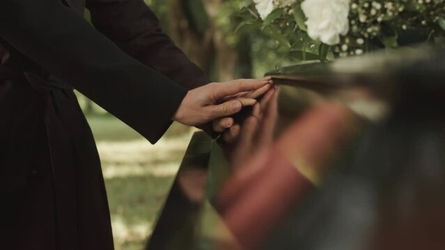 Unrecognizable man putting his hand over female hand touching wooden coffin lid and mourning