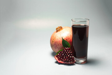 Pomegranate juice in a transparent glass and juicy pomegranate close-up on a light background.