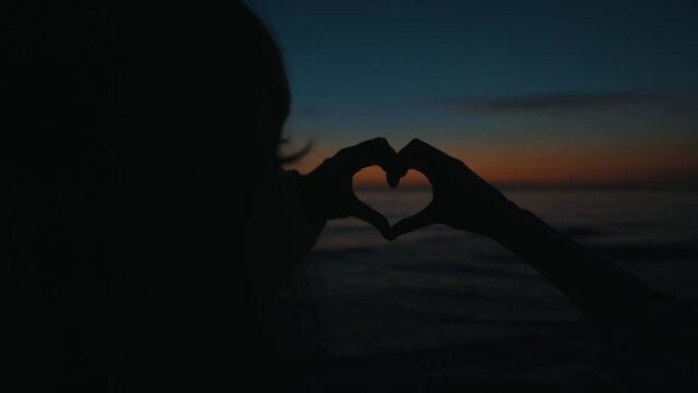 Hands of teenage girl made heart shape at sunset.
