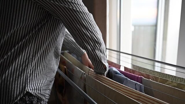 Person taking clothes off expandable drying rack standing near window
