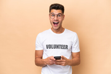Young volunteer caucasian man isolated on beige background surprised and sending a message