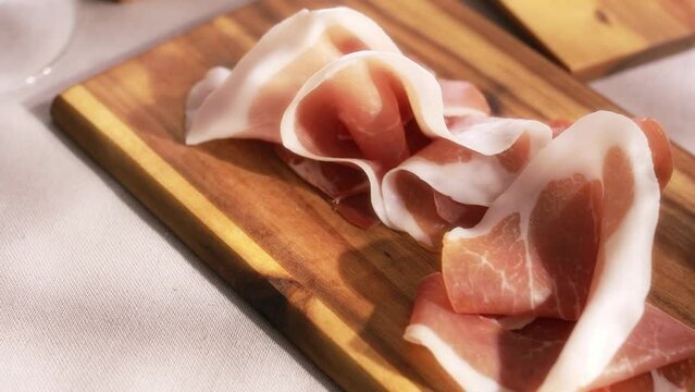 sliced prosciutto on a wooden board in sunny day. pork ham on a light background. composition meat delicacy with olives and bread. High quality 4k footage
