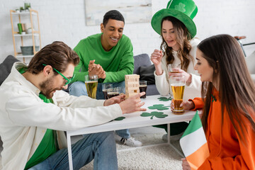 Positive multiethnic friends playing wood blocks game while celebrating saint patrick day at home