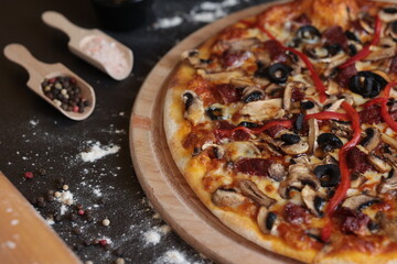 a pizza with mushrooms, olives, and peppers on a table with a spatula