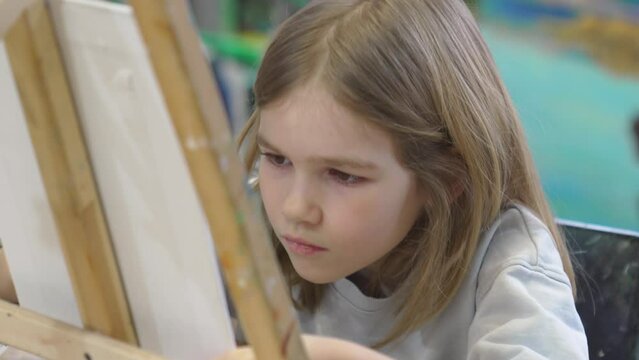 a little girl paints a painting on canvas in an art studio.