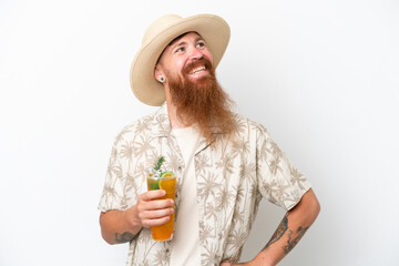 Redhead man with long beard drinking a cocktail on a beach isolated on white background posing with arms at hip and smiling