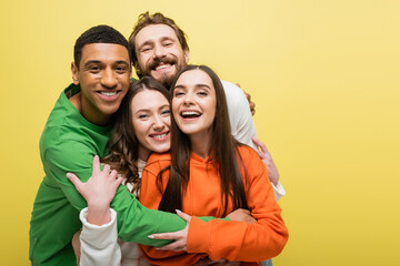 Smiling multiethnic friends hugging isolated on yellow