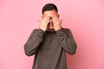 Young Brazilian man isolated on pink background covering eyes by hands