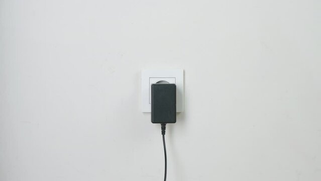 Male hand plugging and unplugging plug into white wall socket. Close-up power socket, caucasian man, charger cable