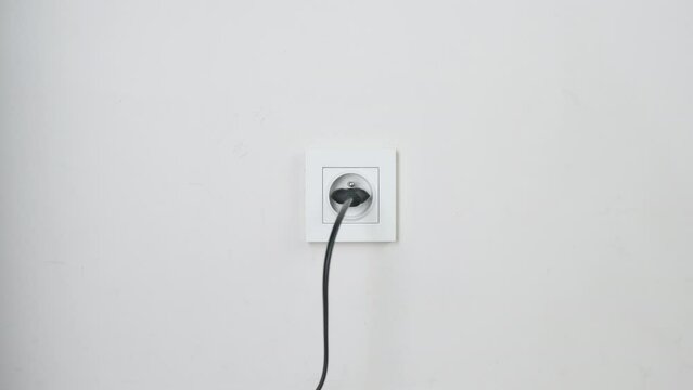 Male hand plugging and unplugging plug into white wall socket. Close-up power socket, caucasian man, charger cable