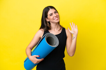 sport Italian woman going to yoga classes isolated on yellow background saluting with hand with happy expression