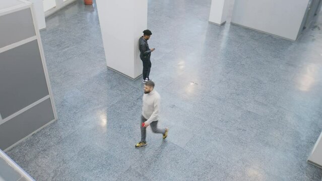 People walk at office building lobby. African American man stands and surfs the internet. Multi ethnic friends meet. Monitoring and CCTV technology. Concept of social safety. Security camera shooting.