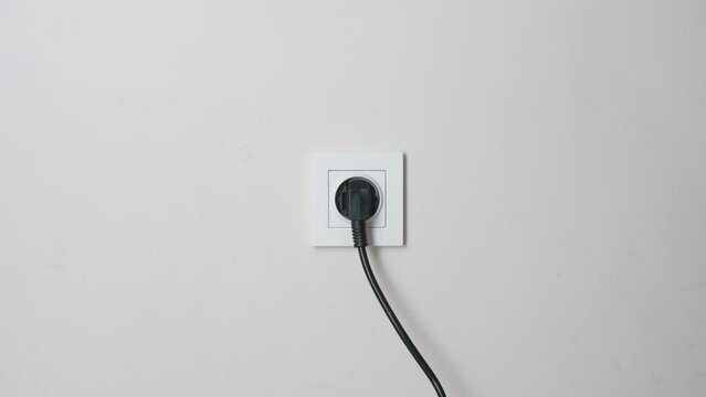 Male hand plugging and unplugging plug into white wall socket. Close-up power socket, caucasian man, charger cable