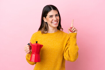 Young Italian woman holding a coffee maker isolated on pink background pointing up a great idea