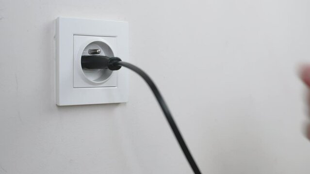 Male hand plugging and unplugging plug into white wall socket. Close-up power socket, caucasian man, charger cable