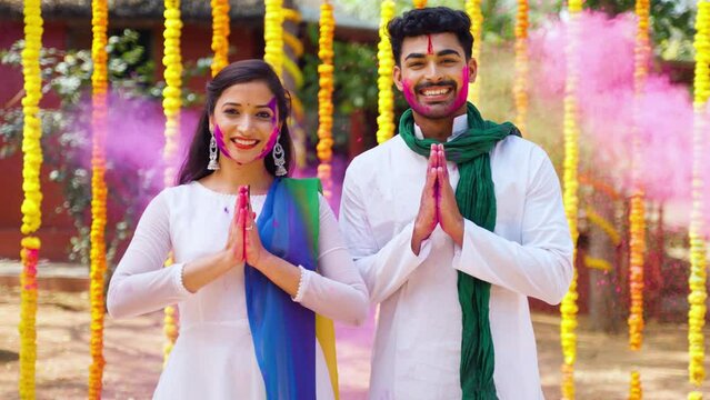 Happy young couple with color on face saying namaste againt flower decorated background - concept of holi festival greeting, wishes and Indian. traditional culture