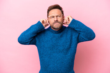 Middle age caucasian man isolated on pink background frustrated and covering ears