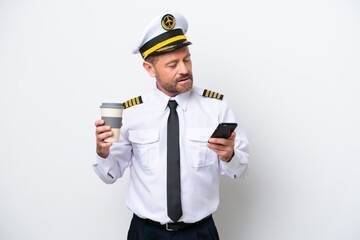Airplane middle age pilot isolated on white background holding coffee to take away and a mobile © luismolinero