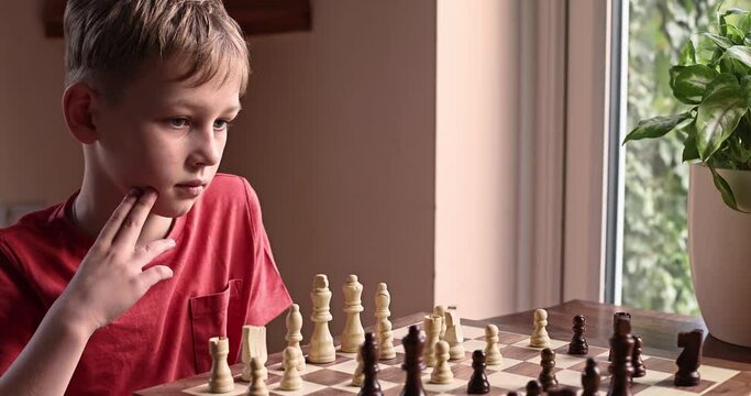 Young white child playing a game of chess on large chess board. Chess board on table in front of school boy thinking of next move, tournament