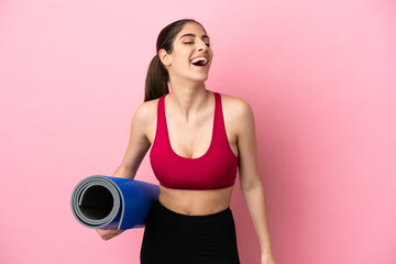 Young sport caucasian woman going to yoga classes while holding a mat laughing