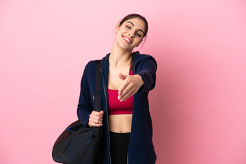 Young sport caucasian woman with sport bag isolated on pink background shaking hands for closing a...