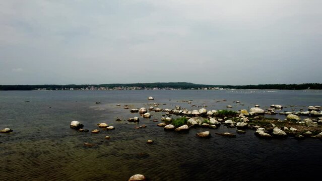 Aerial arc shot over rocky coastline with white boulders scattered in the sea bay on the coast of sweden, view of the port city H&auml;llevik, forests and the baltic sea with calm waves and clear water