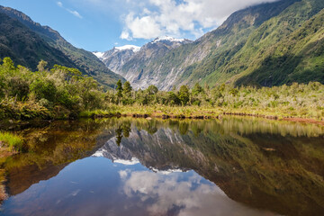 Fototapeta na wymiar Peters Pool, a mirror lake, reflecting the snow capped mountains at Franz Josef on the South Island of New Zealand