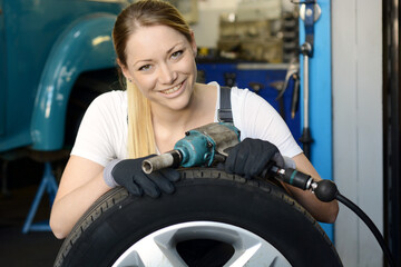 Female mechanic servicing car tire on aluminium rim in car garage - 570275224