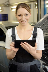 Female car mechanic repairing and servicing and inspecting car in garage using diagnostic device on...